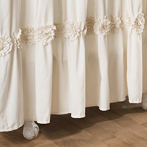 Cream curtain with ruffled floral accents on wooden floor.